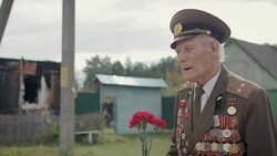 An elderly gray-haired veteran of the great Patriotic war and world war II in uniform with many badges and orders goes through the village. Grandpa is in the hands of red carnations Stock Footage
