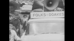 1960s: Car with speakers on roof drives down street Stock Footage