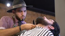 Young barber trimming beard of client in salon Stock Footage