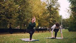 Female yoga instructor is teaching starting student Eagle pose in park, cheerful girl is making mistakes and laughing, women are enjoying nature and exercise. Stock Footage
