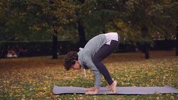 Beautiful brunette is practising Bakasana balancing on hands on yoga mat exercising alone in park. Modern youth, recreational activity and leisure concept. Stock Footage