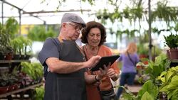 Salesman help senior woman with tablet at flower shop Stock Footage