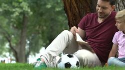 Father and son reading book after active football match, family communication Stock Footage