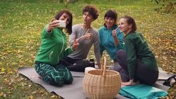 Pretty young women are taking selfie with smartphone during picnic in park sitting on grass, posing and laughing having fun. Nature, friendship and technology concept. Stock Footage