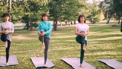 Female yoga students are doing balancing exercise standing on one leg on mats in park, girls are training under guidance of professional instructor. Stock Footage