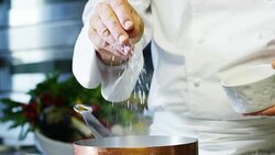 in an Italian professional kitchen a chef pours salt on a dish or in the water to boil the Italian pasta concept of healthy and light food. Stock Footage