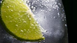 Macro close-up,refreshing soda tonic fizzy water, lime in Glass, ice. Slice of lemon, mineral bubbles. Detox or thirst concept. Healthy, dietary nutrition. Cold lemonade mojito drink. Black background Stock Footage