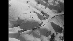 California, 1952: A man measures almost 20 feet of snowfall as the Donner Pass, connecting San Francisco and Chicago, is barely seen at bird's eye view Stock Footage