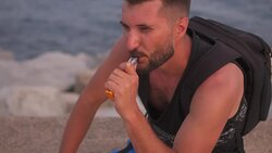 Thoughtful bearded man vaping cigarette while sitting on beach Stock Footage