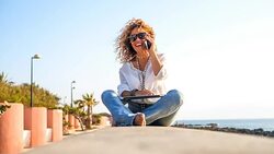 Front view of a pretty young woman with curly hair, talking at the phone at the beach,with laptop for outdoor work Stock Footage