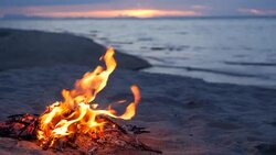 Blazing campfire on the beach during summer evening. Bonfire in nature as background. Burning wood on white sand shore at sunset. selective focus. tropical romantic landscape near sea water edge. Stock Footage