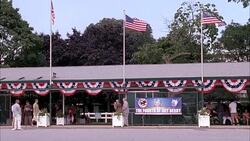 WIDE ANGLE OF ENTRANCE TO MONMOUTH PARK, HORSE RACING TRACK IN OCEANPORT, NEW JERSEY. SIGN FOR THE FOURTH OF JULY DERBY. PEOPLE, PEDESTRIANS, SPECTATORS. AMERICAN FLAGS. Stock Footage