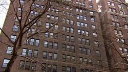 PAN UP OF MULTI-STORY APARTMENT BUILDING. COULD BE CONDOMINIUMS IN DOWNTOWN CITY URBAN AREA. CAMERA PANS DOWN AND ZOOM IN TO ENTRANCE AT STREET LEVEL WITH CARS PARKED IN FRONT. SHOT REPEATS. Stock Footage