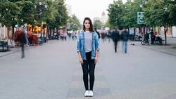 Time-lapse portrait of stressed young woman standing alone in city center wearing jeans and denim jacket and looking at camera while people are passing by. Stock Footage