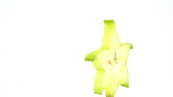 Half frame of one star shaped slice of ripe carambola fruit with water drops. Slowly rotating on the turntable isolated on the white background. Close up. Macro. Copy space. Stock Footage
