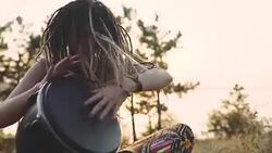 Beautiful young hippie woman with dreadlocks playing on djembe. Funky woman drumming in nature on an ethnic drum at sunset or sunrise Stock Footage