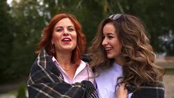 SLOW MOTION: Two young women cute communicate with each other. The weather is cold, so women hide behind a plaid. Women smile when communicating. Stock Footage