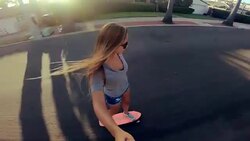 Point of view shot of happy girl riding skateboard down street at sunset holding selfie camera Stock Footage