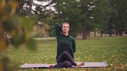 Cheerful lady is exercising in park sitting in Cow Face pose with arms behind her back during outdoor practice in city park. Nature, millennials and health concept. Stock Footage