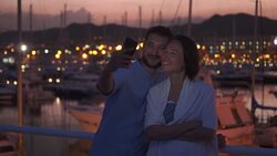 Positive couple in love taking photos in the evening against harbour Stock Footage
