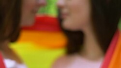 Beautiful lesbians wrapping in rainbow flag, making heart with hands and kissing Stock Footage